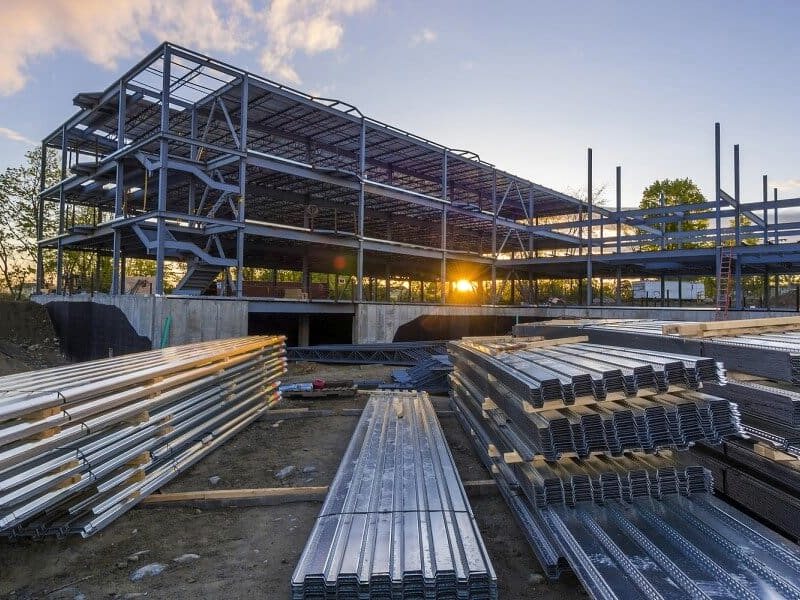 Structural steel frame of a commercial building under construction, with steel studs stacked on site