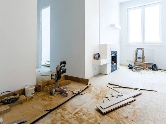 Interior of a home mid-renovation with the subfloor exposed and trim removed