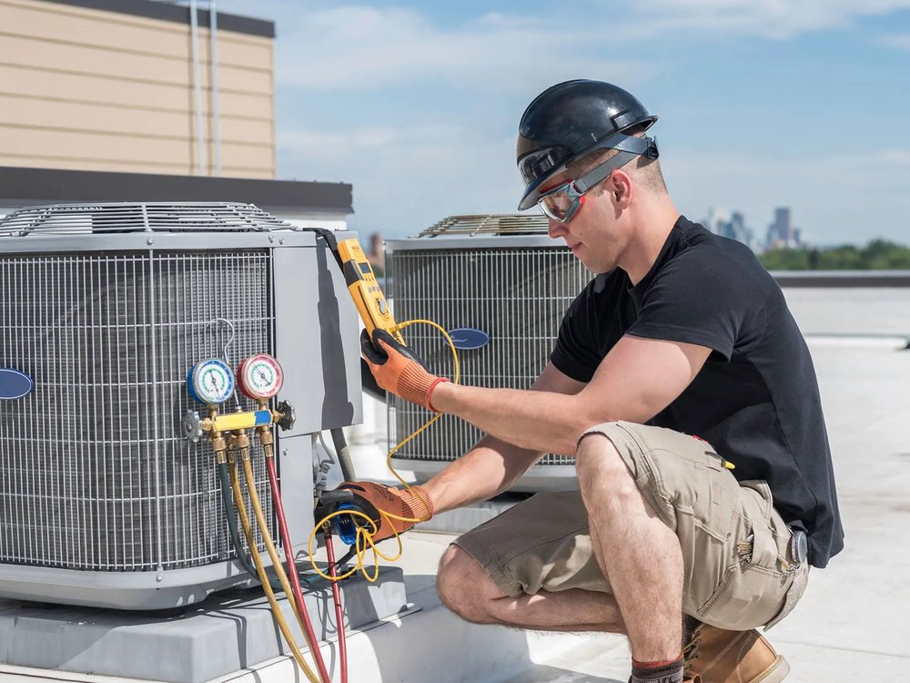 HVAC technician using manifold gauges to service a rooftop condenser unit