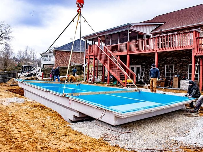 Pool shell being lowered by crane into an excavated backyard